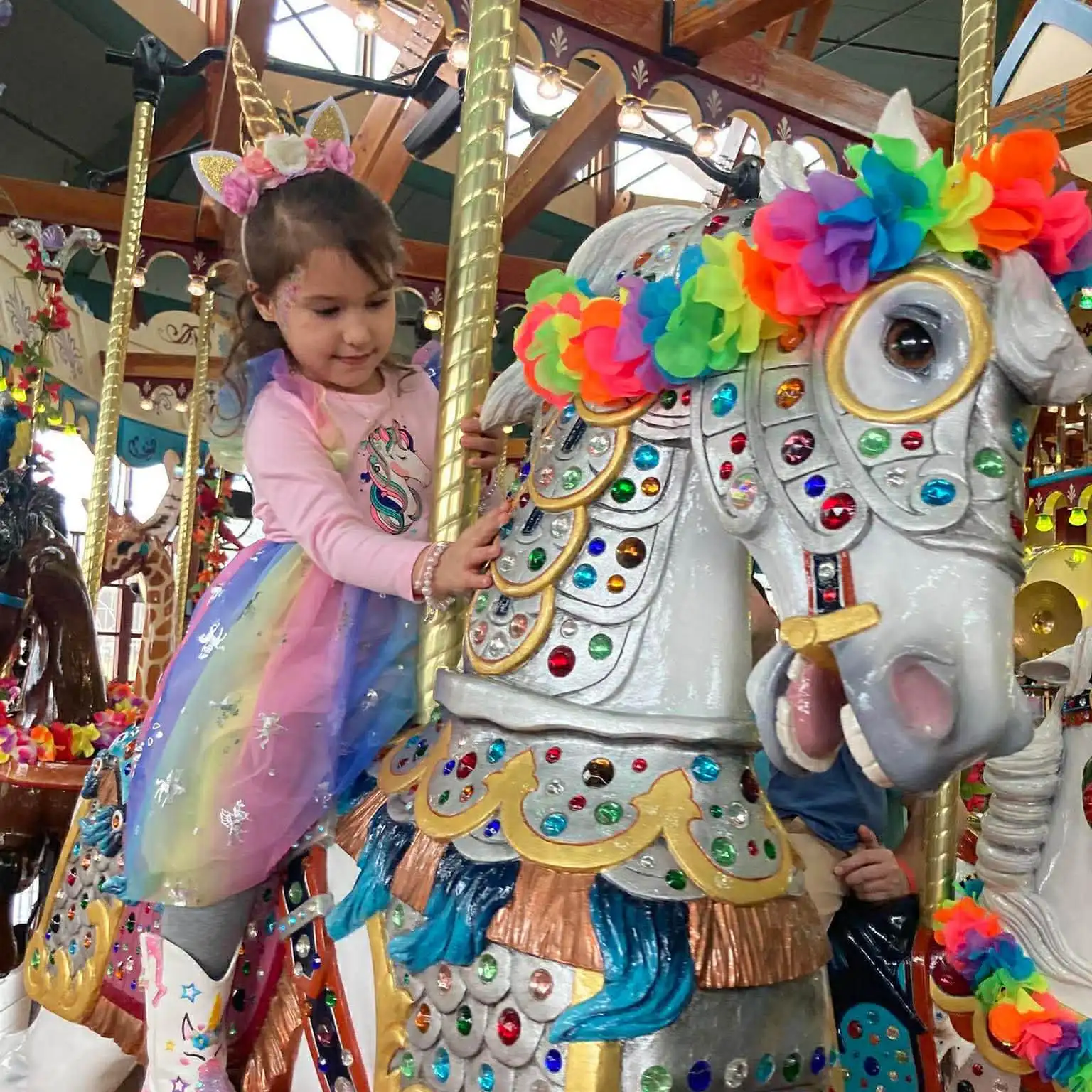 A child wearing a unicorn dress riding a carousel horse.