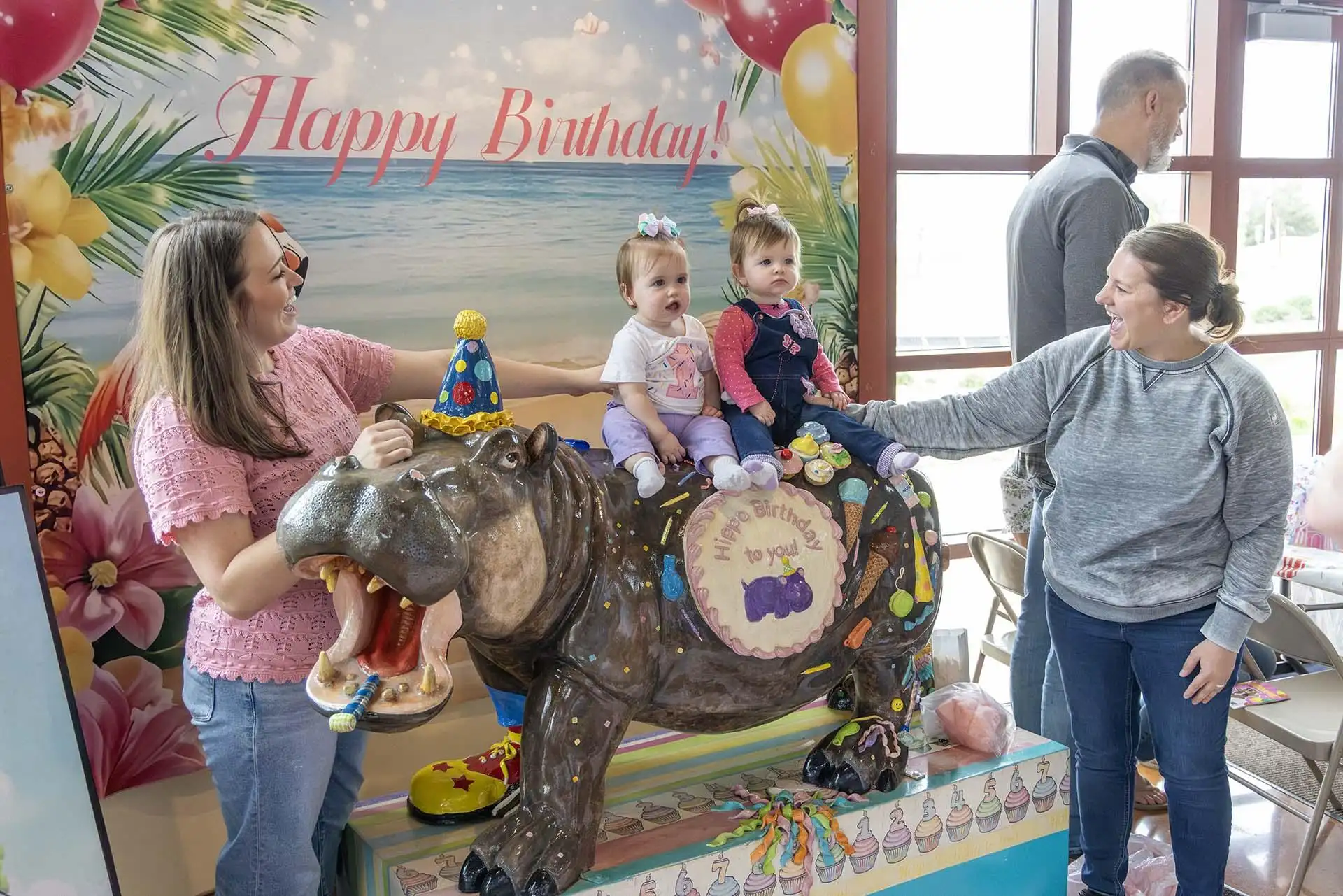 Two children sit atop the Birthday Hippo at the Silver Beach Carousel, assisted by their parents.