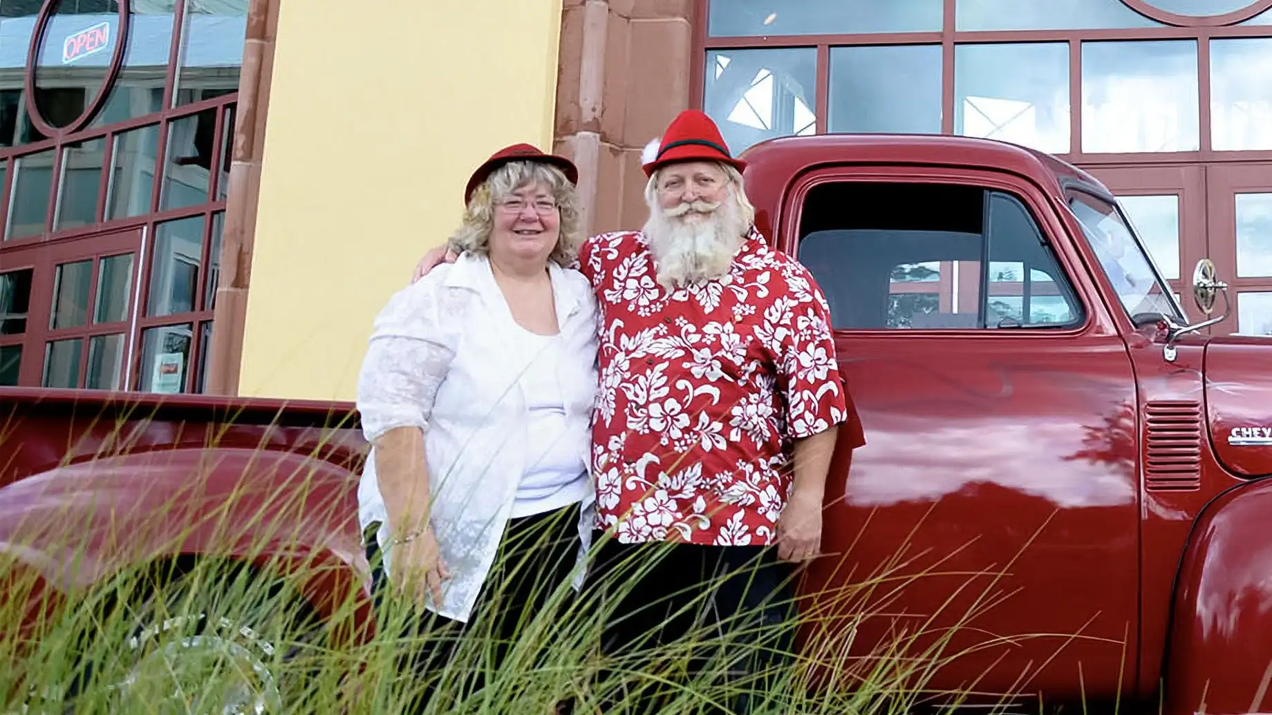 Santa and Mrs. Claus stand beside a classic red truck in front of the Silver Beach Carousel.